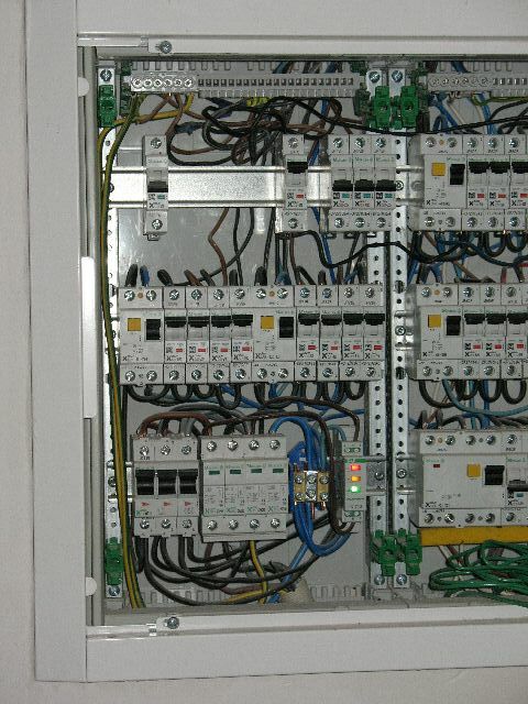 Otwarta skrzynka elektryczna z bezpiecznikami, przewodami i listwami zaciskowymi, widoczne diody sygnalizacyjne.